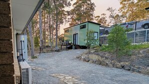 A gravel driveway leading to a modern house with a small deck, a water tank, and a power generator. - 3BR Bushland Retreat, Relax/ Professional Stay–near the bay & CBD/ Private Deck (North Batemans Bay)