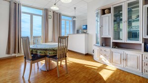 Een eethoek met een ronde tafel, stoelen, een televisie en een kast met glazen deuren.