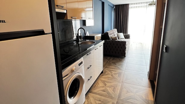 A modern kitchen with a washing machine, a dining area with a sofa, and a hallway leading to a door. - HAYAL LARA DELUXE APART OTEL (Antalya)