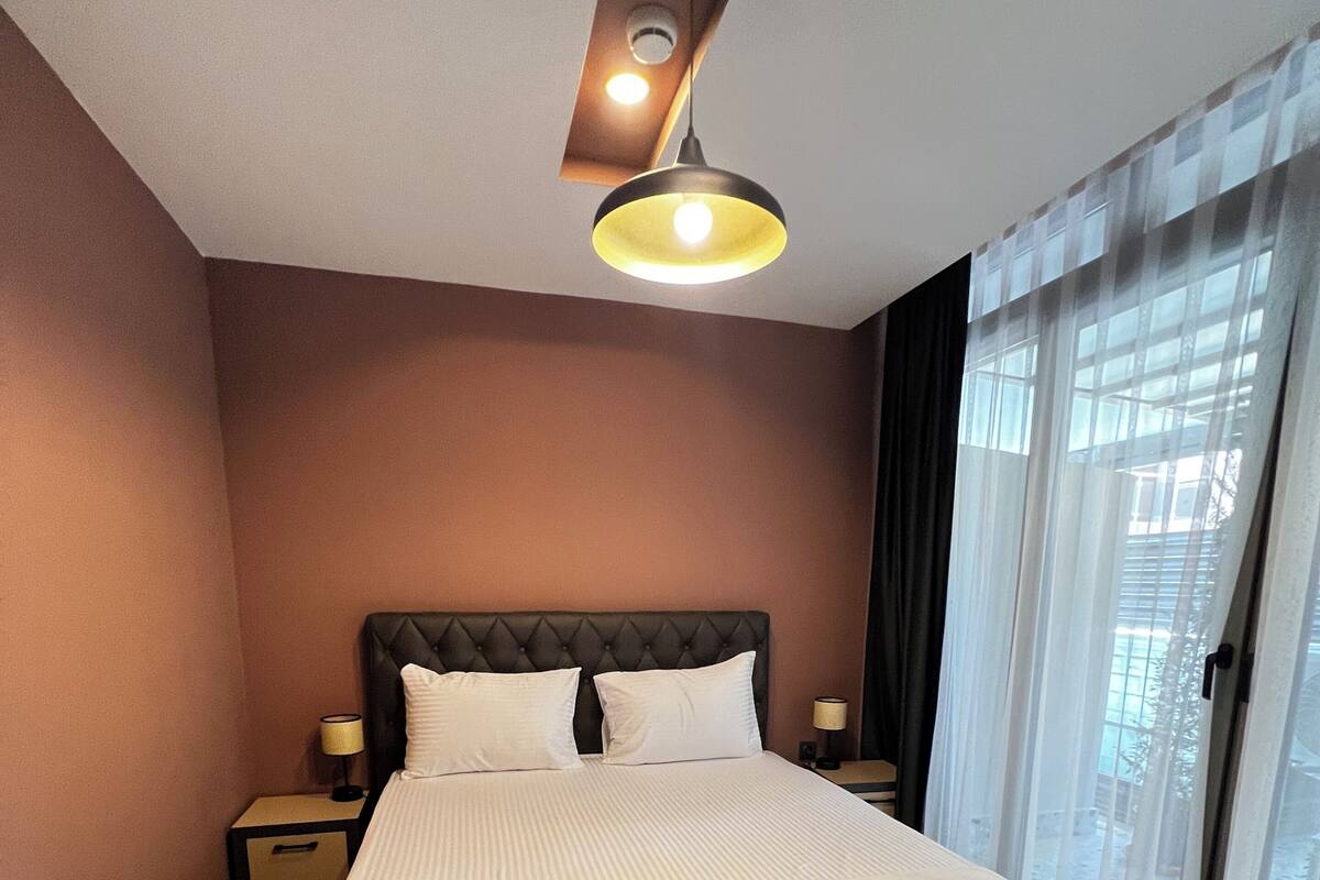 A hotel room with a large bed, a nightstand, a lamp, and a window with curtains.