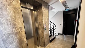 A modern elevator with a marble wall, a staircase with a metal railing, and a door marked 'EXIT'. - HAYAL LARA DELUXE APART OTEL (Antalya)