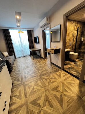 Una habitación de hotel con piso de diseño geométrico, una cama, un escritorio, un televisor, un espejo y un baño con ducha.
