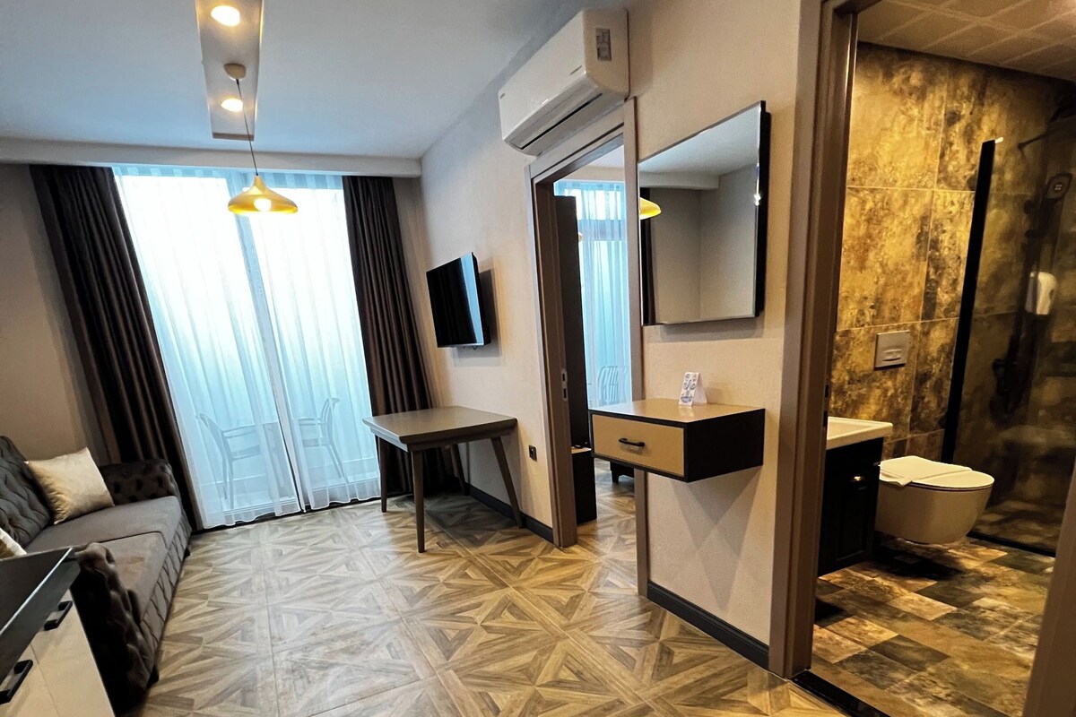 A hotel room with a geometric patterned floor, a bed, a desk, a TV, a mirror, and a bathroom with a shower.