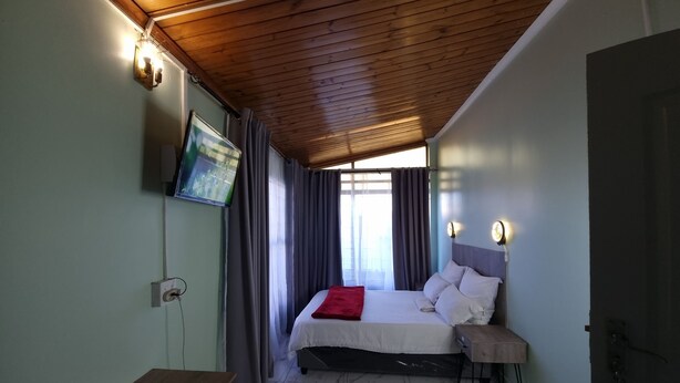 A room with a bed, a desk, a TV mounted on the wall, and a window with curtains.