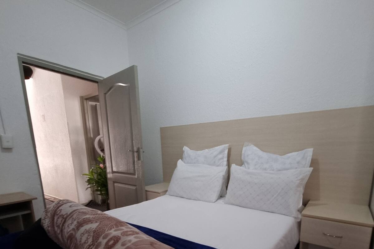 Ein Hotelzimmer mit einem Bett, einem Nachttisch, einer Tür und einer Pflanze.