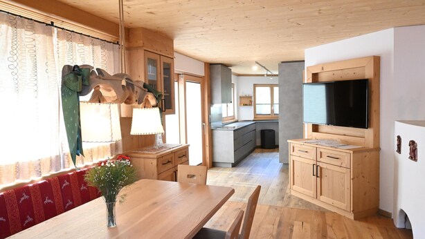Un intérieur en bois comprenant une table à manger, des chaises, un téléviseur et un coin cuisine.
