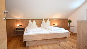 Une chambre à coucher avec un lit en bois, deux tables de chevet avec des lampes, une tête de lit en bois et une petite table ronde sur laquelle est posé un vase.