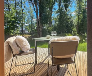 Eine Holzterrasse mit zwei Stühlen und einem Tisch, mit Blick auf ein bewaldetes Gebiet.