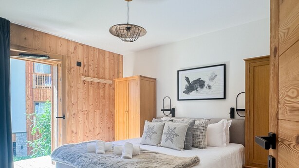 A bedroom with a bed, a wooden wardrobe, a framed picture on the wall, and a door leading to an outdoor area. - K1 facing the slopes ski in / ski out Megève (Megève)