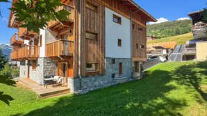 A multi-story wooden building with balconies, stone foundation, and a grassy yard. - K1 facing the slopes ski in / ski out Megève (Megève)