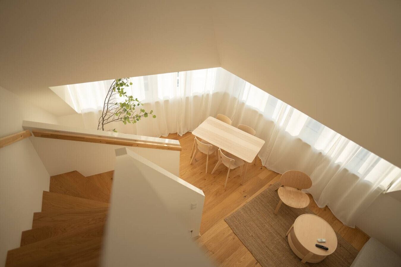 A modern interior with a wooden staircase, a dining area with a table and chairs, and a small round table with a remote control.