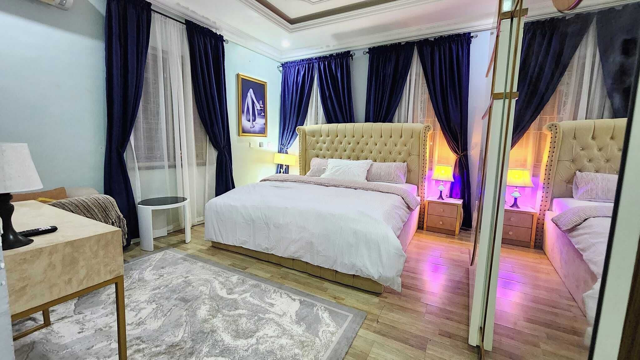 Una habitación de hotel con una cama grande, dos mesitas de noche con lámparas, una pequeña mesa redonda y una silla.