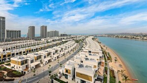Un quartier résidentiel en bord de mer, avec des immeubles d’appartements modernes, une plage et un ciel dégagé.
