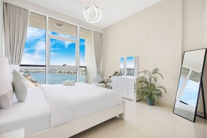 A bedroom with a large bed, a dresser, a mirror, and a potted plant. - FIRST CLASS |1BR| Sea View Paradise | Scenic Views (Ras Al Khaimah)