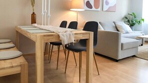 Ett modernt vardagsrum med ett matbord i trä, svarta stolar, en grå soffa och abstrakt väggkonst.