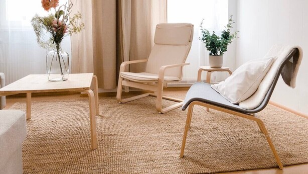 Ett rum med en beige fåtölj, ett litet bord, en krukväxt och en vas med blommor.