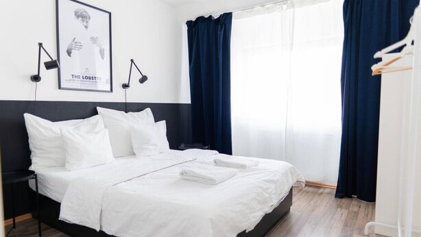A neatly made bed with white linens, a black headboard, and a framed picture on the wall. - White and black by Prater #40 (Vienna)