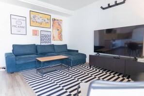 Ein modernes Wohnzimmer mit einem blauen Sofa, einem Holztisch, einem schwarz-weißen Streifen Teppich, einem Flachbildfernseher und Kunstwerken an der Wand.