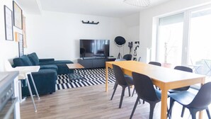 Ein modernes Wohnzimmer mit einer Couch, einem Fernseher, einem Esstisch mit Stühlen und einem gemusterten Teppich.