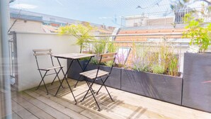 Eine Holzdielen-Terrasse mit Tisch und Stühlen, umgeben von Pflanzen und Blick auf Gebäude.