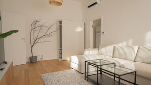 A modern living room with a white sofa, a glass coffee table, a potted plant, and a white cabinet. - Cozy Penthouse with a terrace by Schönbrunn Palace (Vienna)
