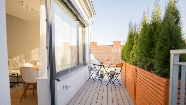 A balcony with a wooden floor, a table with chairs, and a view of the cityscape. - Cozy Penthouse with a terrace by Schönbrunn Palace (Vienna)