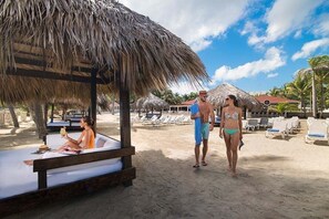 Ein Strand mit Reetdachschirmen, Liegestühlen und einer Holzumkleidekabine.