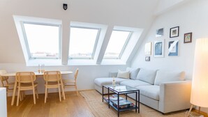 A modern living room with a white sofa, a glass coffee table, and a dining area with wicker chairs. - Two leveled Penthouse Schönbrunn (Vienna)