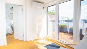 A modern room with a wooden floor, a bed, a large sliding glass door leading to an outdoor deck with plants and a view of a building. - Two leveled Penthouse Schönbrunn (Vienna)