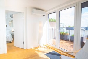 A modern room with a wooden floor, a bed, a large sliding glass door leading to an outdoor deck with plants and a view of a building. - Two leveled Penthouse Schönbrunn (Vienna)