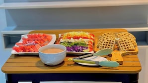 Een houten tafel met diverse soorten eten, waaronder plakjes watermeloen, een kleurrijke salade, wafels en een kom soep.