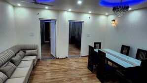 A room with a wooden floor, a sofa, a dining table with chairs, and a ceiling fan. - Hazy hill  (Mussoorie)