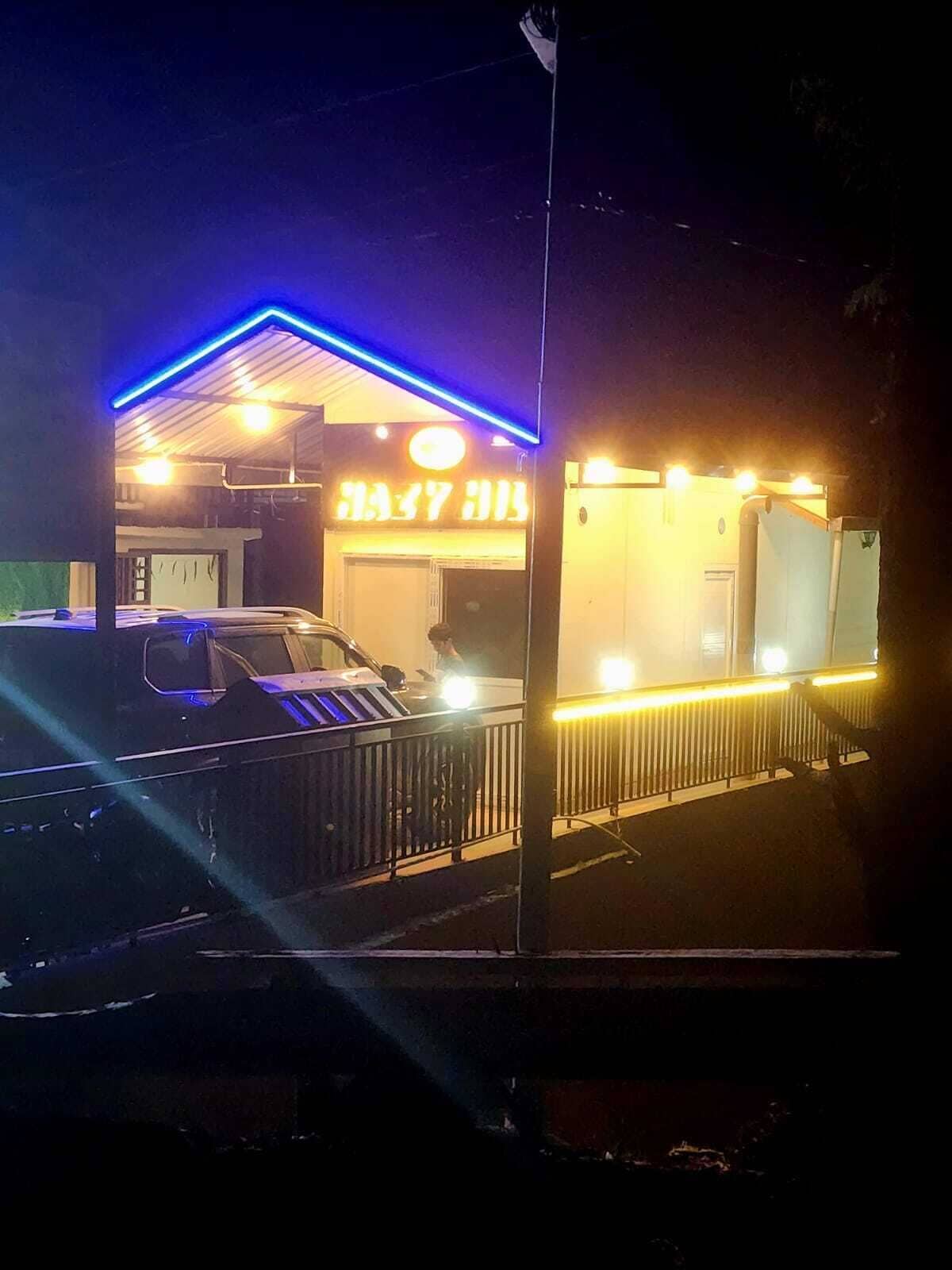 A building with a neon sign, a car parked in front, and a fence.