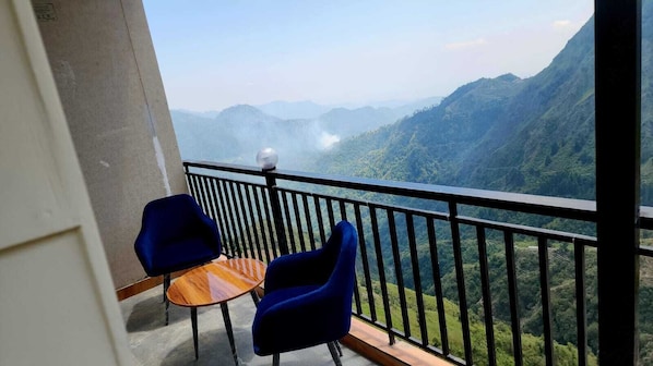 A balcony with a table and two chairs, overlooking a mountainous landscape.