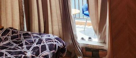 A room with a bed, a wooden wardrobe, and a balcony with a chair.