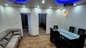 A spacious living area with a sofa, dining table, chairs, and a ceiling fan. - Hazy hill  (Mussoorie)