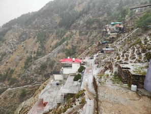 A mountainous area with buildings, including a house with a red roof and a multi-story structure with a green roof. - Hazy hill (Mussoorie)