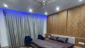 A bedroom with a bed, a desk, a chair, a wardrobe, and a ceiling fan. - Hazy hill  (Mussoorie)