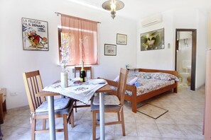Una habitación con una cama, una mesa con sillas, un ventanal con cortinas, una pared decorada con cuadros y un aire acondicionado.