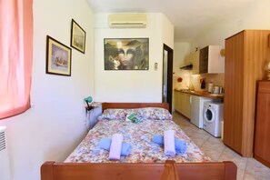 A bedroom with a bed, a nightstand, a wall-mounted air conditioner, and a view into the kitchen area. - Cozy studio with garden terrace in Zambratija (Zambratija)