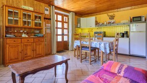 A wooden interior with a dining table, chairs, a bench, and a kitchen area with cabinets and appliances. - Gîte "À l’ombre du Tilleul": Mountain View, Private Terrace & Wi-Fi (Montpezat-sous-Bauzon)