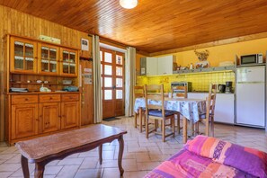 A wooden interior with a dining table, chairs, a bench, and a kitchen area with cabinets and appliances. - Gîte "À l’ombre du Tilleul": Mountain View, Private Terrace & Wi-Fi (Montpezat-sous-Bauzon)