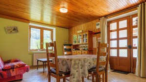 A wooden-paneled room with a dining table, chairs, a sofa, and a window with a view of trees. - Gîte "À l’ombre du Tilleul": Mountain View, Private Terrace & Wi-Fi (Montpezat-sous-Bauzon)