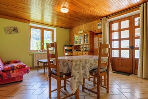 A wooden-paneled room with a dining table, chairs, a sofa, and a window with a view of trees. - Gîte "À l’ombre du Tilleul": Mountain View, Private Terrace & Wi-Fi (Montpezat-sous-Bauzon)