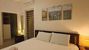Ein Hotelzimmer mit einem großen Bett, einem Nachttisch mit Lampe, einer Klimaanlage, einem Kleiderschrank und einem Kunstwerk an der Wand.