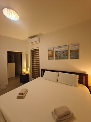 A hotel room with a bed, a nightstand, a lamp, an air conditioning unit, a wardrobe, and artwork on the wall. - Modern 2BR APT in Central Birkirkara (Mgarr)