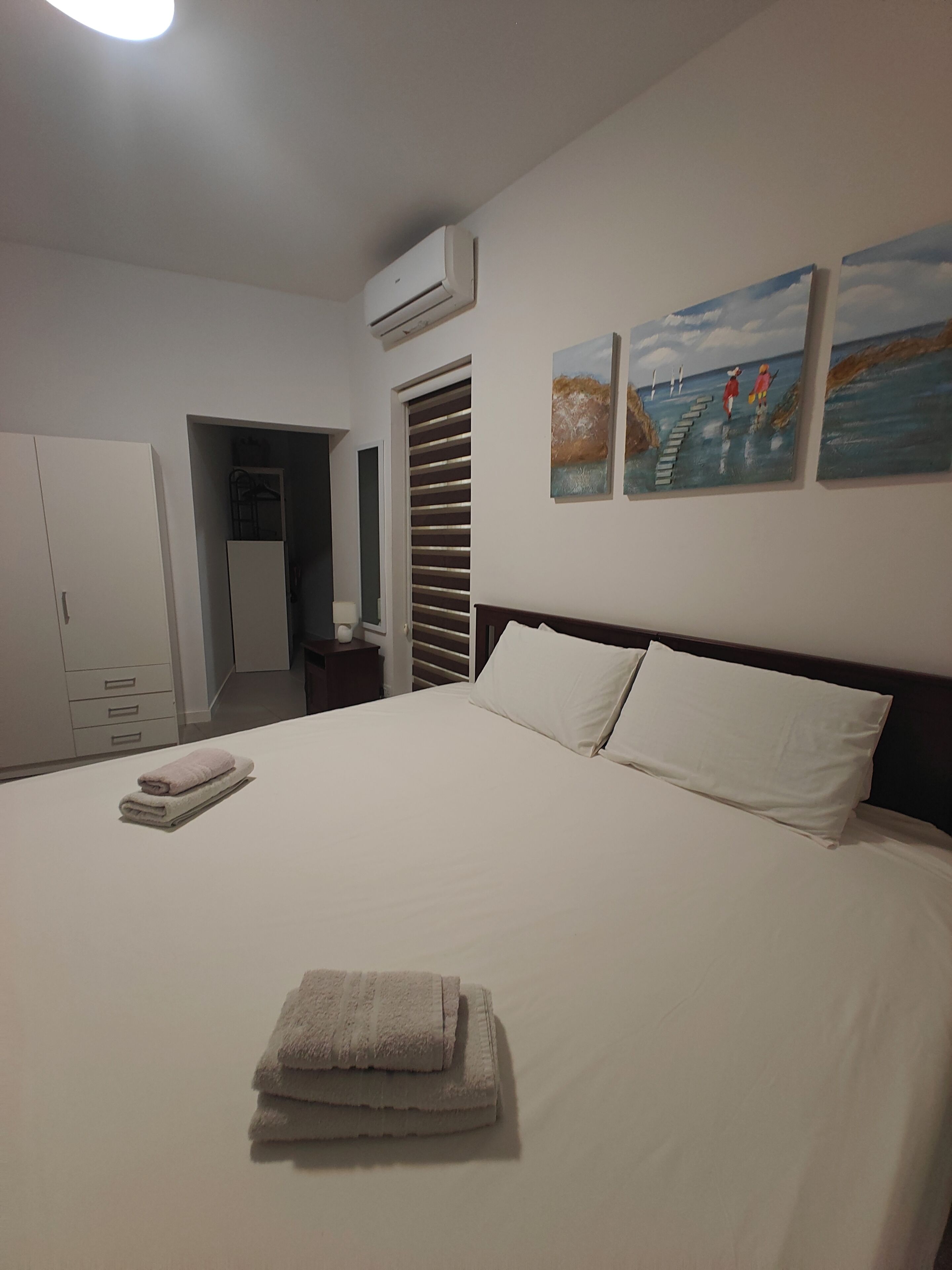 Une chambre à coucher avec un lit, une armoire, une porte et deux tableaux accrochés au mur.