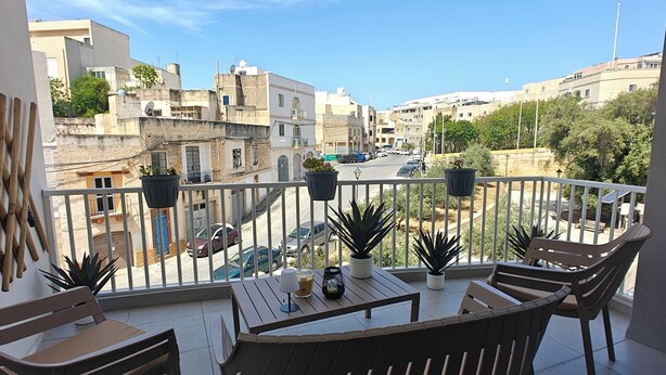 Ein Balkon mit Tisch, Stühlen, Topfpflanzen und Blick auf eine Stadtansicht.