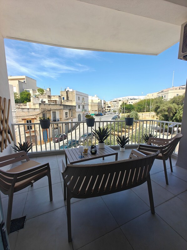 A balcony with a table, chairs, potted plants, and a view of a cityscape.