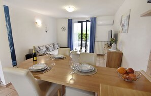 Ein Essbereich mit einem Holztisch, gedeckt für vier Personen, einer Couch mit gemusterten Kissen, einer Vase mit Blumen und einer Obstschale auf dem Tisch.